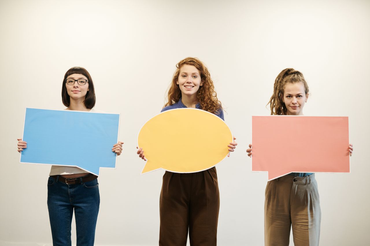 Three women holding colorful speech bubbles, expressing creativity in a studio setting.