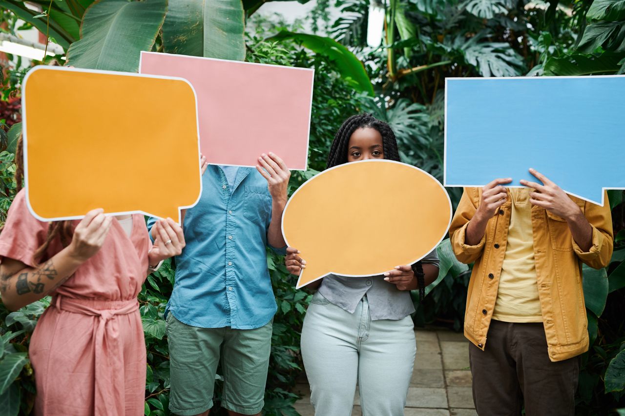 A group of adults holding colorful speech bubble signs in a lush greenhouse setting.